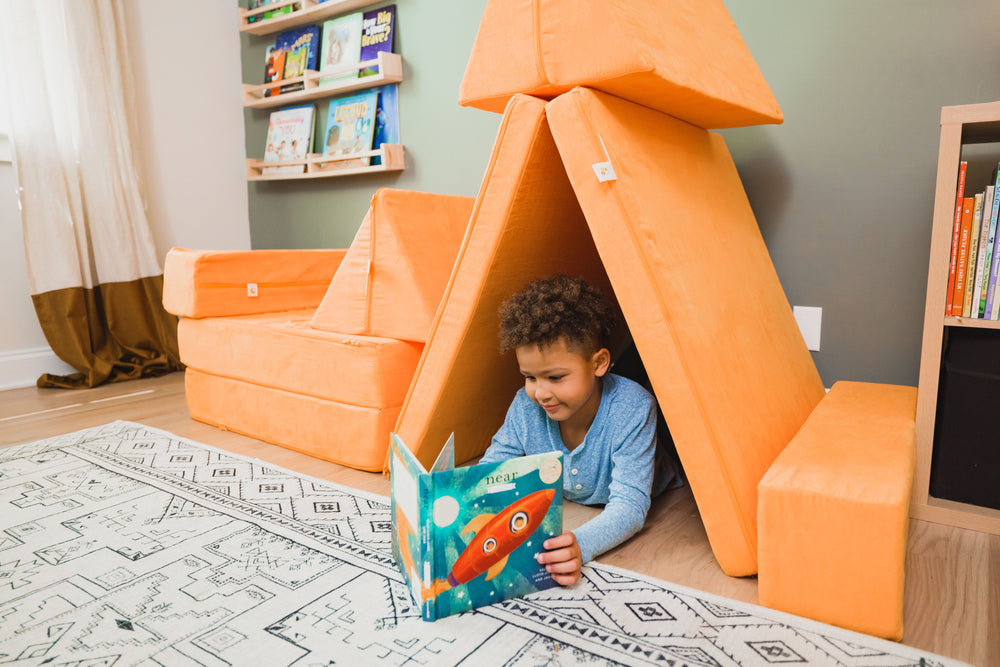Child reading inside an orange FoamOh Super Castle fort in a living room
