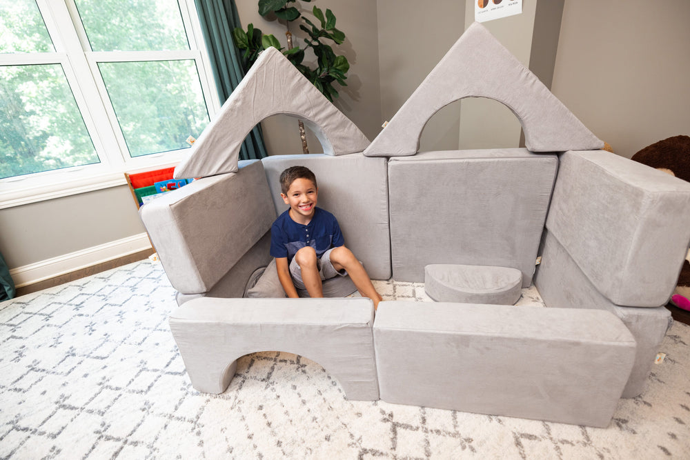 Child sitting inside a light grey FoamOh kids castle couch fort