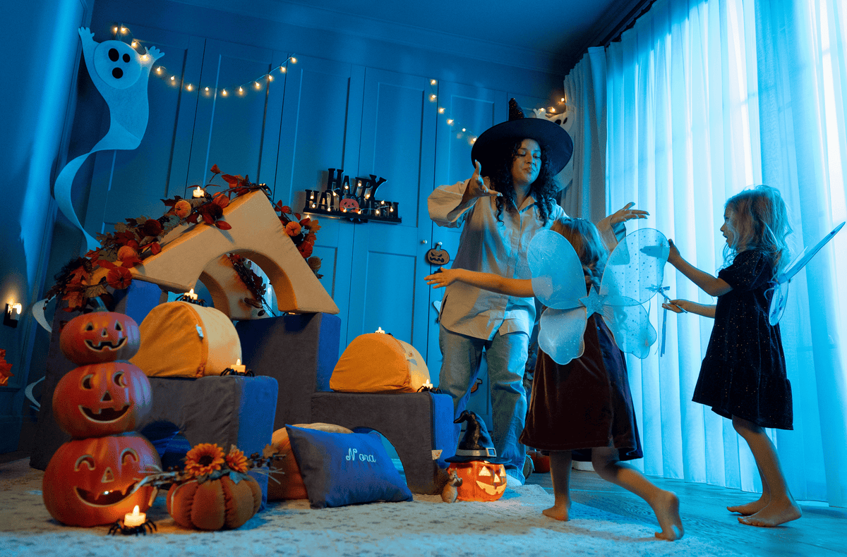 Kids in witch and fairy costumes play with a FoamOh foam castle fort decorated with Halloween pumpkins.